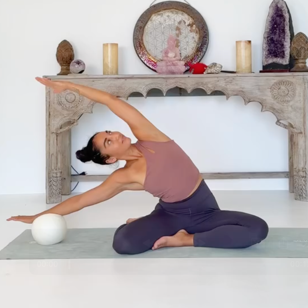 women in side bend stretch with crossed legs and using a Pilates ball to deepen the stretch