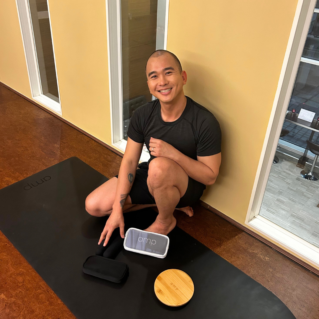 Tim yoga and pilates teacher sitting on an amp wellbeing mat with wrist weights and core sliders