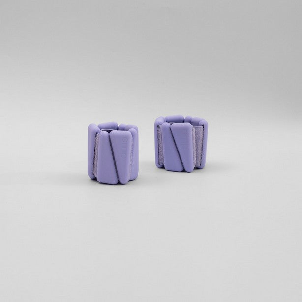A pair of purple adjustable ankle wrist weights placed on a white surface.