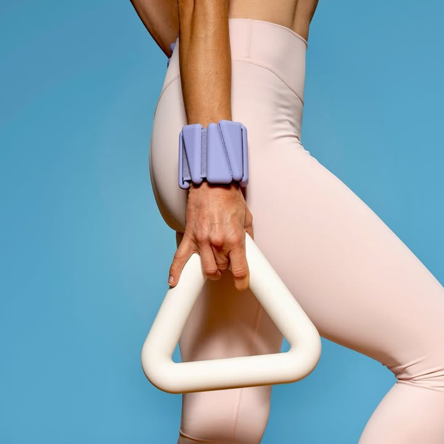 Person wearing light pink leggings holding a white and purple exercise triangle weight against a blue background