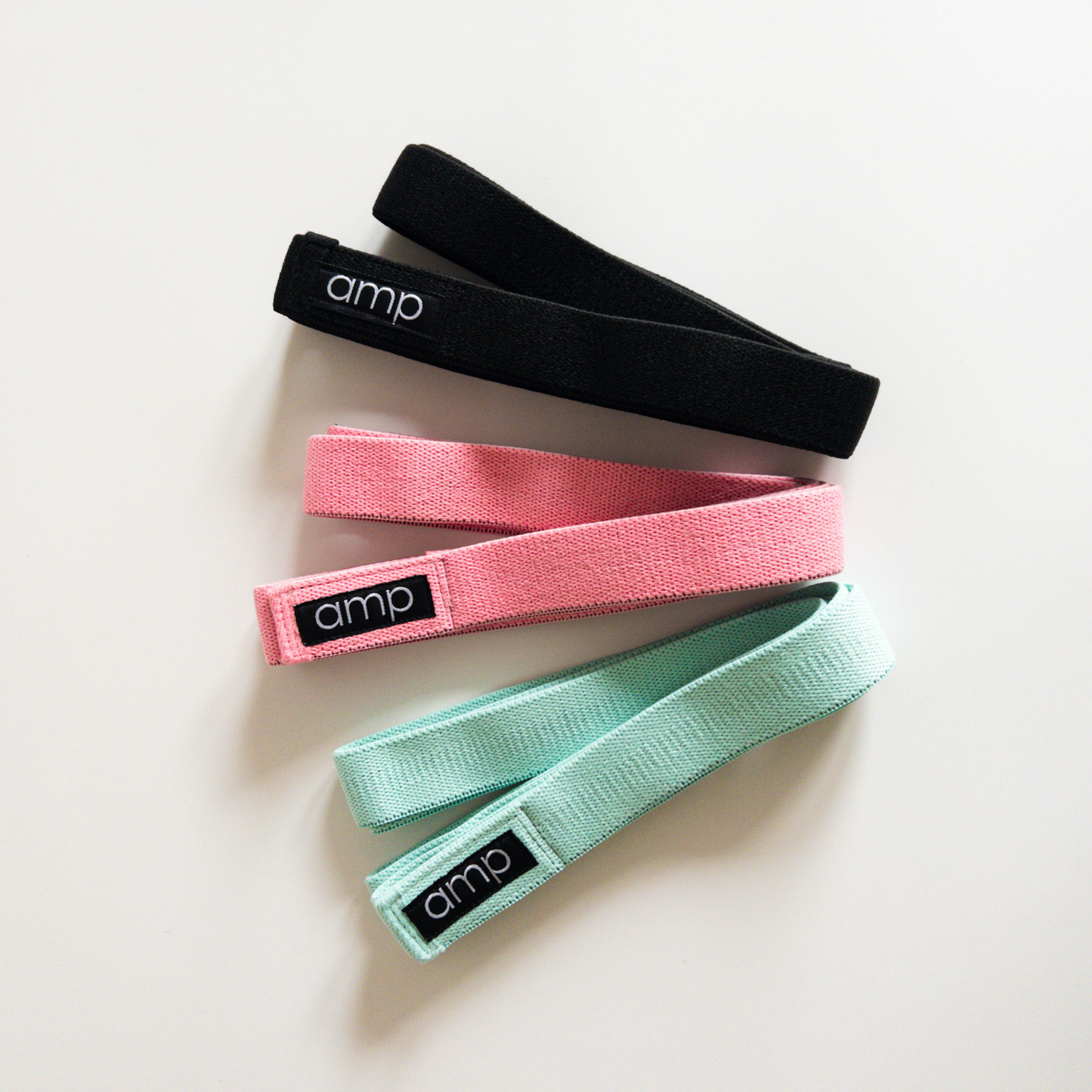 Three exercise bands in black, pink, and green with 'amp' branding 