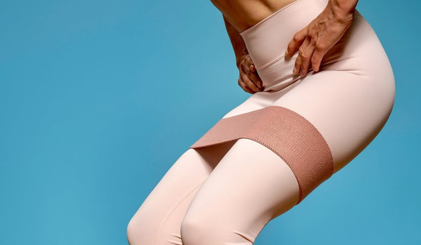 Person wearing beige leggings with a brown band against a blue background