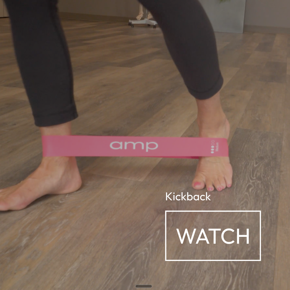 A pink Amp resistance band wrapped around a person's feet on a wood-look floor, with the text 'Kickback' and 'WATCH' overlaid on the image.