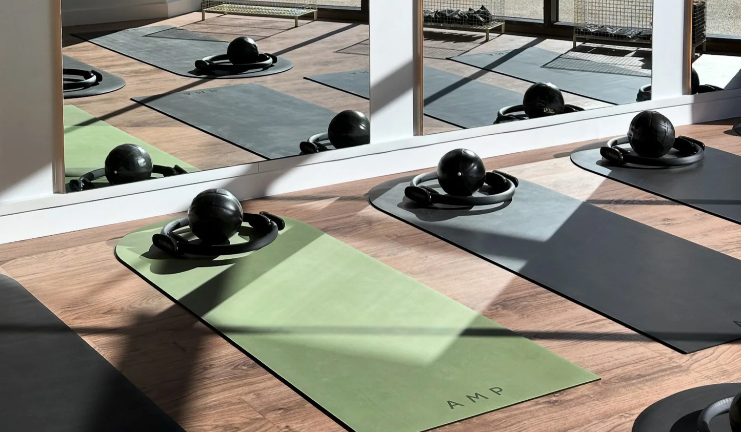 Yoga mats and exercise balls arranged on a wooden floor with yoga and pilates mats with mirrors in the background.