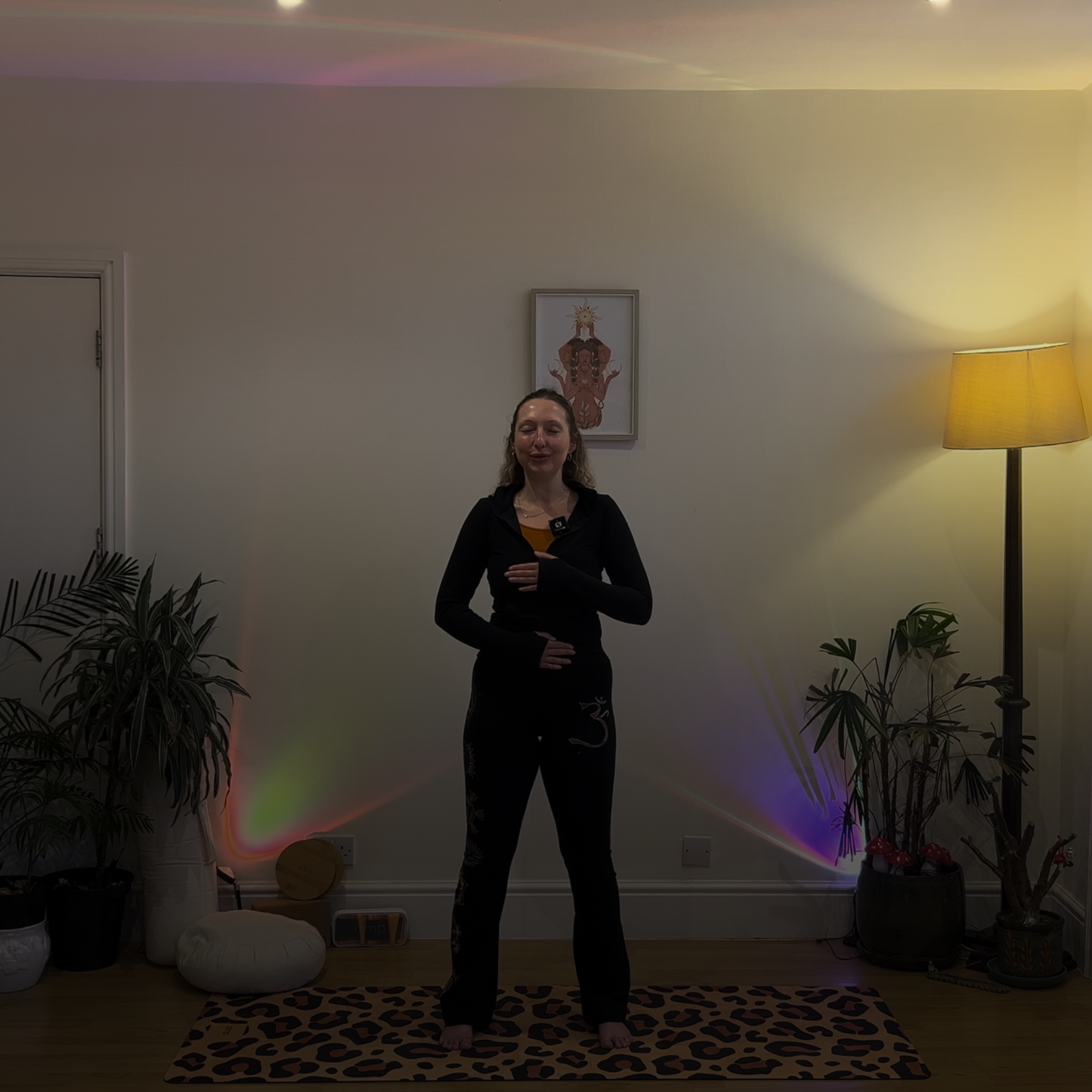 Person standing in a room with plants and a lamp, with a colorful light projection on the wall. breathwork and yoga with amp wellbeing